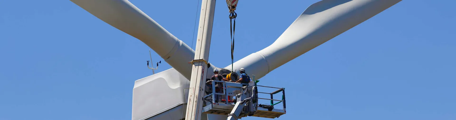 Techniker warten eine Windturbinennabe in schwindelerregender Höhe, gesichert durch Sicherheitsgurte und Helme